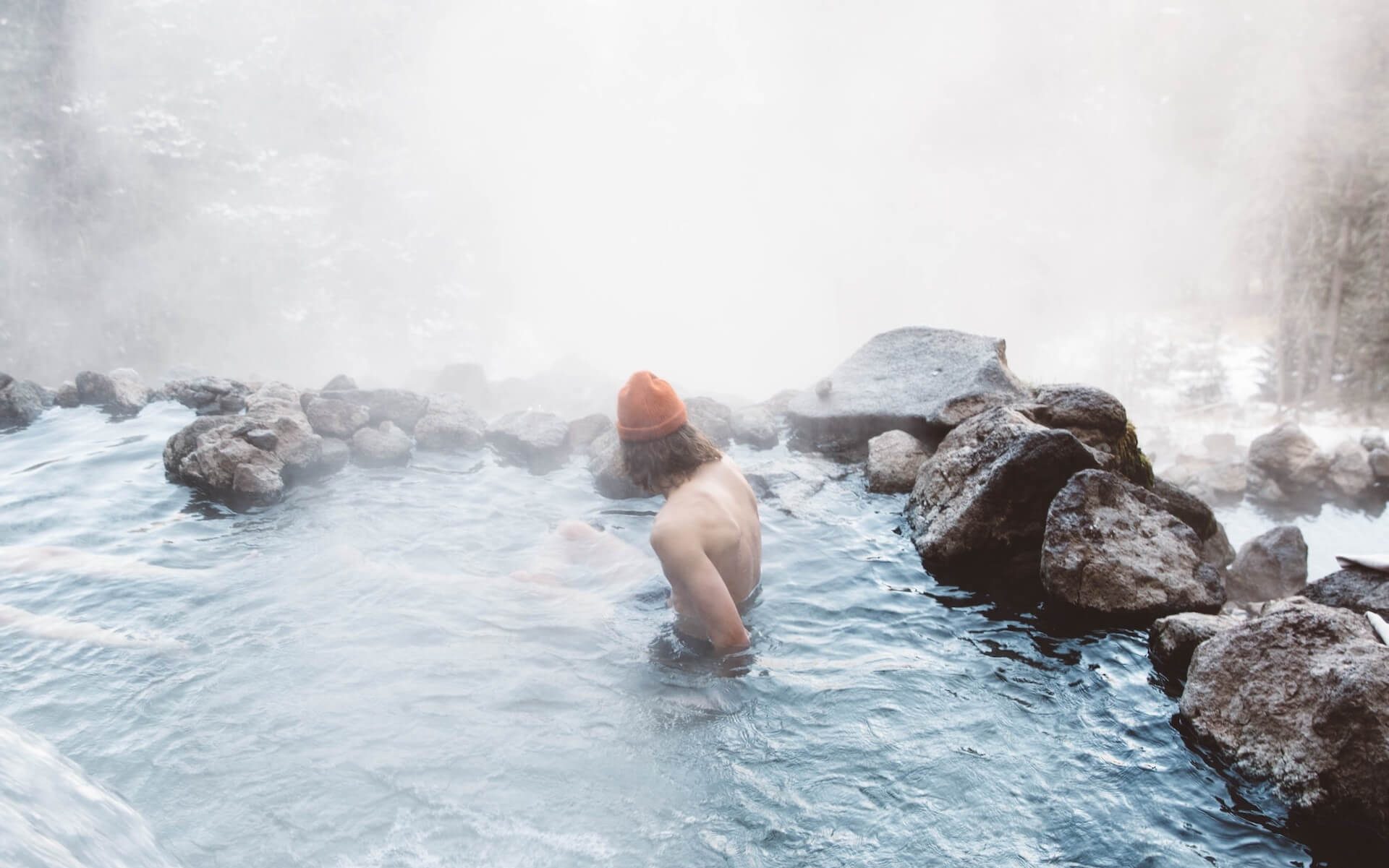 Person enjoying a hot spring in a snowy environment.